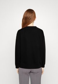 Schwarzes Sweatshirt mit Rundhalsausschnitt und gerippten Bündchen, von hinten gezeigt. Glatte Textur, lässige Passform, kombiniert mit hellgrauen gerippten Hosen.