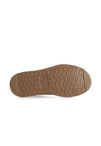 Tan gummiskosula med vågig slitbana. Har ett logotyptryck och texturerade områden. Sammanlagt slät med svagt upphöjda sektioner.