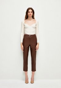 Haut crème à manches longues et col bateau associé à un pantalon cropped en simili cuir marron taille haute avec une fermeture à double bouton.