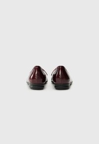 Chaussures en cuir bordeaux avec une finition brillante, bout rond et semelle en caoutchouc noir basse. L'arrière présente un design simple et épuré.
