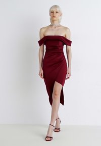 Robe bordeaux à encolure Bardot avec une silhouette ajustée, fente sur le côté, texture satinée lisse et ourlet à hauteur de genoux.