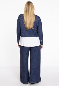 Denim spijkerjack met lange mouwen en een cropped ontwerp, gecombineerd met losse denim broek, beide in donkerblauw. Kenmerkt zich door gouden stiksels.