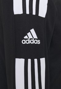 Svart atletisk skjorta med vit tre-stripesdesign på axlarna och en vit Adidas-logga på bröstet. Materialet är slätt och stretchigt.