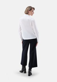 Blusa bianca a maniche lunghe con colletto a punta, abbinata a pantaloni a gamba larga blu navy e stivaletti neri. Tessuto liscio e vestibilità sartoriale.