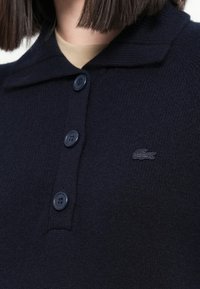 Maglione lavorato a maglia blu navy con colletto, dotato di cinque bottoni e un piccolo logo ricamato sul petto. Texture morbida e design classico.