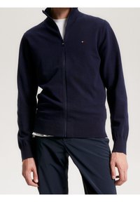 Suéter de cremallera en color marino, confeccionado con tejido suave, con un alto cuello y puños acanalados. Pequeño logo en la parte superior izquierda.