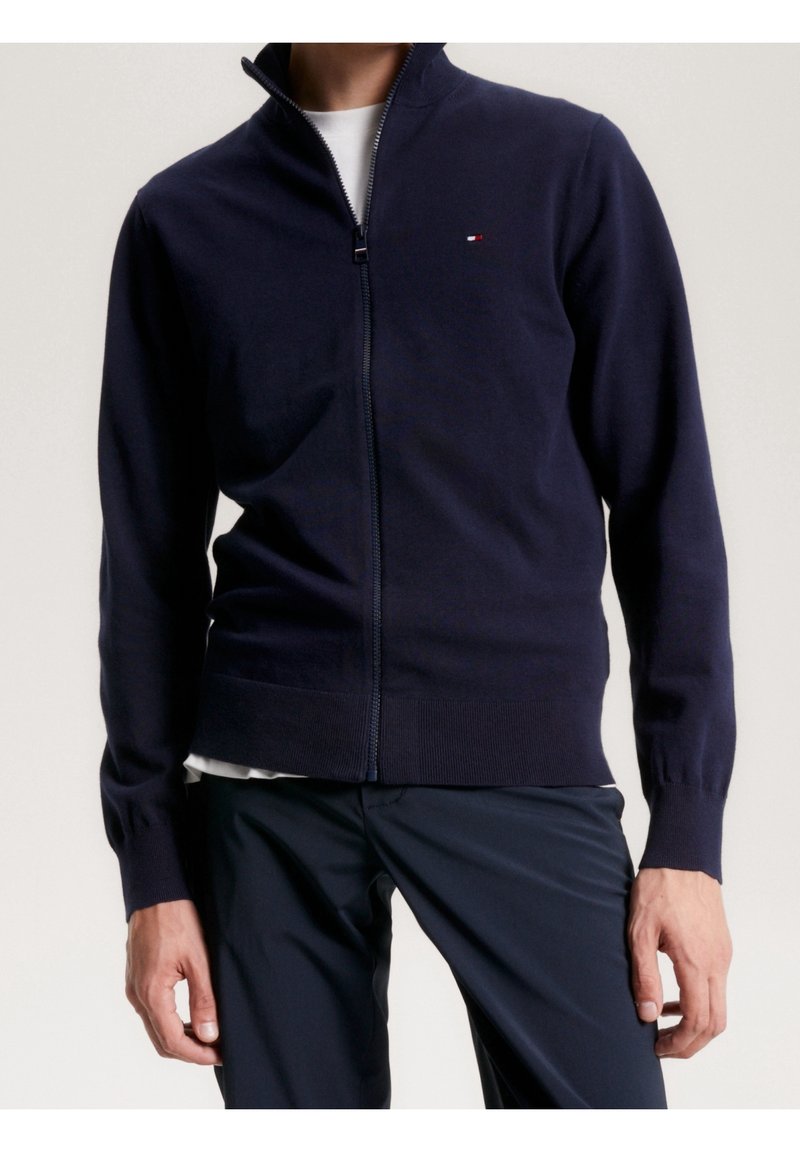 Suéter de cremallera en color marino, confeccionado con tejido suave, con un alto cuello y puños acanalados. Pequeño logo en la parte superior izquierda.