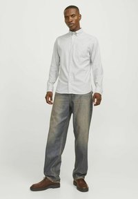 Biała koszula zapinana na guziki z delikatnymi pionowymi paskami, połączona z luźnymi, wyblakłymi niebieskimi dżinsami i brązowymi butami na sznurówki. Teksturowana tkanina.