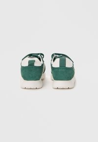 Sneakers verde in suede con dettagli bianchi, forma arrotondata, finitura testurizzata e lacci a contrasto. Presenta una linguetta sul tallone per facilitare l'indossare.