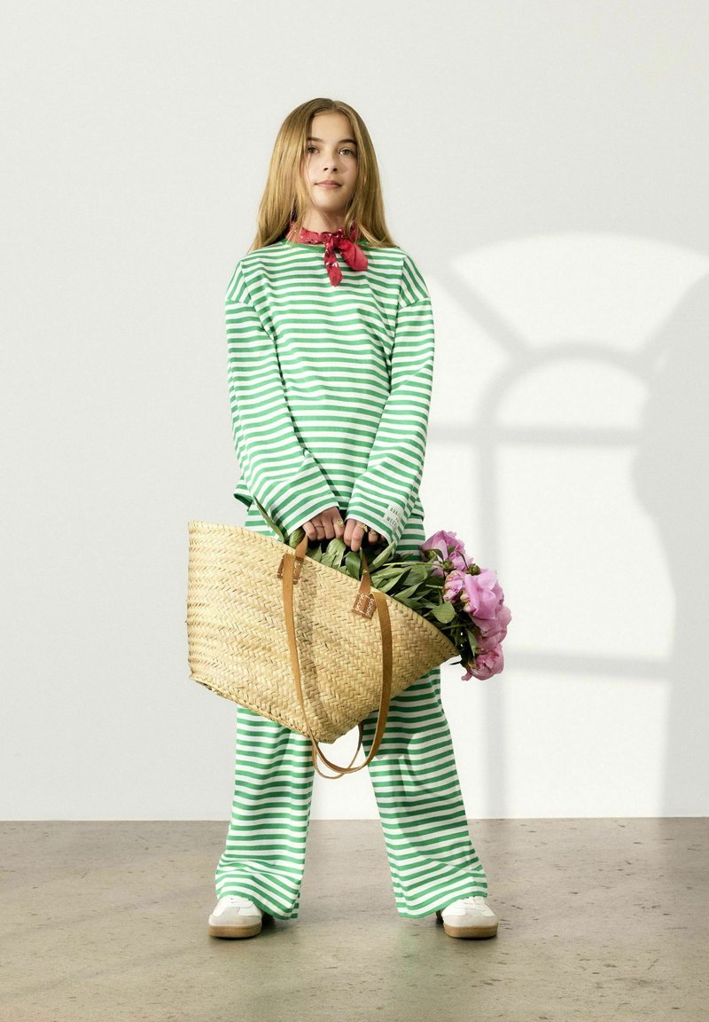 Tenue rayée verte et blanche comprenant des manches longues et un pantalon ample. Le sujet tient un sac en osier avec des fleurs roses.