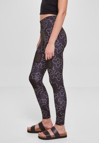 Crne leggings s bijelim cvjetnim uzorkom, s mrežastim panelima. Uparene s tamnim sandalama; glatka tekstura i prilagođen oblik.