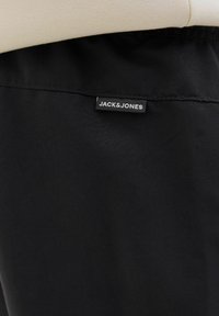 Czarne szorty z gładkiego materiału z elastyczną talią. Zawierają białą metkę z logo "JACK & JONES" przyszytą do pasa.