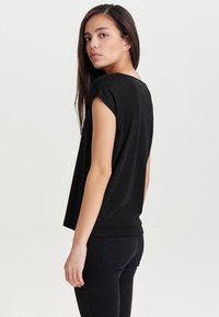 Sort kortærmet t-shirt med rund hals, blød tekstur, løs pasform og en let længere bagkant, båret med sorte jeans.
