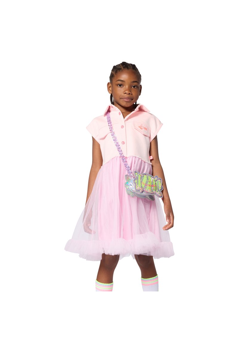 Ροζ φόρεμα πόλο με κοντά μανίκια και φούστα από τούλι, συνδυασμένο με ολογραφική τσάντα χιαστί και ριγέ κάλτσες μέχρι το γόνατο.