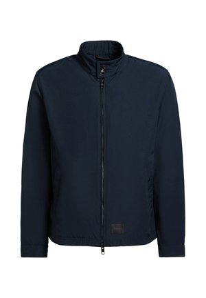 Chaqueta ligera azul marino con cuello alto, cremallera frontal, correa de cuello con botón y mangas largas, con la etiqueta "KHUJO" en el dobladillo.