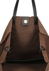 Bruine suède tote bag met zwarte leren handvatten, voorzien van een magnetische sluiting en een binnenzak met gouden hardware-details.