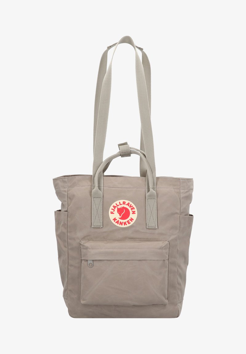 Grijze canvas draagtas met twee handvatten aan de bovenkant en lange schouderbanden, met een voorvak en een ronde logopatch.