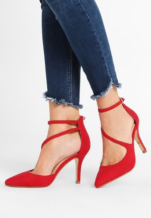 Czerwone zamszowe szpilki z wyciągającym noskiem, paskiem na kostce i cienką szpilką. Posiadają gładką teksturę i złoty akcent na obcasie.
