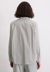 Chemise à manches longues avec un motif géométrique en blanc, or et marron. Présente un col classique et des poignets boutonnés, fabriquée en tissu léger.