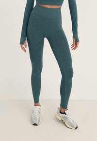 Světlé modré legíny s vysokým pasem a bezešvou konstrukcí, vyrobené z texturované látky, v kombinaci se šedými sportovními botami.