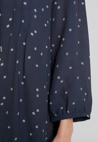 Námořnická modrá blůza s bílým květinovým vzorem, jemná textura, sklady a volné, nařasené tříčtvrteční rukávy s manžetou.