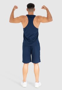Navyblauw tanktop en shorts van ademend materiaal, met een racerback ontwerp, en gecombineerd met witte sportschoenen.
