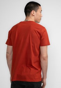 Camiseta roja de manga corta hecha de algodón. Presenta un escote tipo crew, corte relajado y textura suave. Diseño minimalista sin patrones visibles.