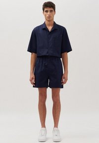 Marineblauw T-shirt met korte mouwen en bijpassende korte broek van lichtgewicht stof, met een zak, elastische tailleband en witte sneakers.