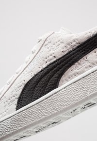 Harmaa mokkanahkakengät, joissa on teksturoitu pinta, ja joissa on voimakas musta nahkastriippi sekä valkea kumipohja.