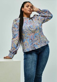 Blå bluse med paisley-mønster og lange pufærmer, med rund halsudskæring og plisserede detaljer, sammen med mørke denimjeans.