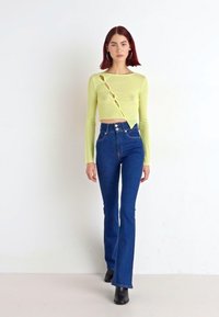 Limegrön långärmad croptopp med urklippning, kombinerad med högmidjade blå utsvängda jeans och svarta ankellångstövlar.