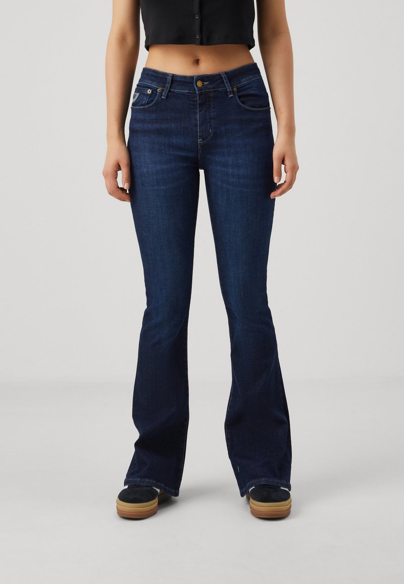 Mörkblå vida jeans med en slät denimstruktur, fem fickor, knäppning med mässingsknapp och markerade sömmar längs med sömmarna.