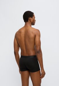 Μαύρα boxer briefs με λείο ελαστικό ζωνάρι στη μέση, ριμπ υφή και εφαρμοστή σχεδίαση, εμφανίζονται από πίσω σε μοντέλο με σκούρο δέρμα.