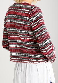 Veste à motifs rouge, noire et blanche avec des designs géométriques ; coupe cropped ; tissu texturé avec un mélange de points et de triangles.