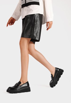 Mocassini neri con plateau realizzati in pelle lucida, con un accento decorativo a catena, dotati di una punta arrotondata e di una suola spessa e testurizzata.