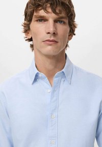 Jasnoniebieska koszula zapinana na guziki, wykonana z gładkiej, lekkiej tkaniny. Posiada klasyczny kołnierzyk oraz małe guziki na przedniej listwie.