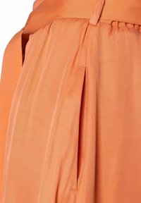 Tissu orange au toucher lisse, présentant des plis et une taille froncée. Un design minimaliste sans matériel visible ni motifs.