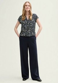 Short-sleeve, navy blouse with a scattered white and green dot pattern, paired with loose-fitting, dark pants and black shoes.