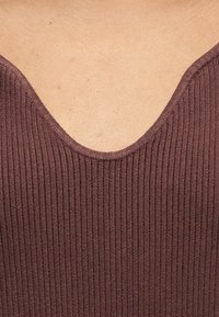 Gros plan sur une encolure de peau nue portant un haut en maille côtelée mauve avec un décolleté en V profond.