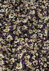 Motif dense de tissu floral avec de petites fleurs violettes, blanches et beiges ainsi que des feuilles vertes sur un fond noir, présentant de légières plis.