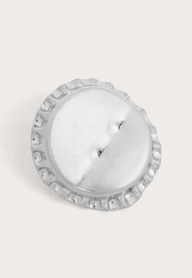 Broche métalique ronde de couleur argentée avec un bord cannelé et une fermeture à épingle à l'arrière, sur un fond neutre.