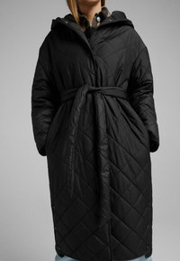 Czarny, pikowany płaszcz z diamentowym wzorem, w talii z paskiem oraz kapturem. Posiada zatrzaski na dole i kieszenie boczne.