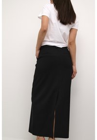 Jupe noire midi avec une fente latérale, coupe ajustée, présentant une texture lisse et un détail à la taille. Associée à un t-shirt blanc simple.