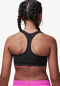 Sutien sport negru cu design racerback. Are o textură netedă și cusături contrastante. Purtat cu pantaloni scurți de antrenament roz.