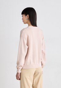 Sweatshirt cor-de-rosa claro com decote redondo, ombros caídos e punhos canelados. O tecido suave apresenta uma textura lisa e um design minimalista.