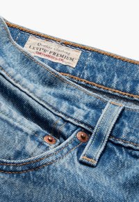 Jeans de denim azul claro con cierres de botones de cobre, costuras marrones y una etiqueta blanca que dice "Levi's Premium, San Francisco, Cal."