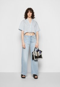 Camisa curta azul clara com riscas, de mangas curtas, combinada com jeans de perna larga em lavagem clara e uma mala de mão com padrão de cobra em preto e branco.