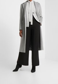 Manteau en laine gris à deux boutons, porté sur un haut gris clair, assorti d'un pantalon large noir et de bottines noires à talons fins.