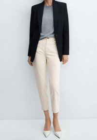 Blazer nero, t-shirt grigia, pantaloni fitted beige chiaro e tacchi bianchi a punta. Tessuto morbido, taglio su misura e linee pulite.