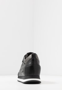 Svart och grå lädersneaker med en mjuk textur, som har en vit mellansula och subtila paneldetaljer. Bakifrån framhävs designens konturer.